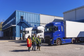 Logistics team in high visibility vests walking and talking beside refrigerated semitrailers at a
