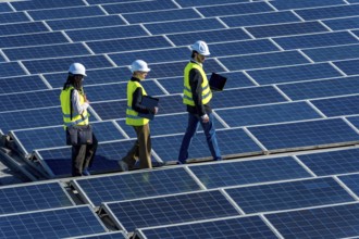 Engineers in hard hats and vests walking on a large solar panel array, inspecting the installation