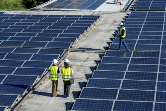 Engineers in hard hats and safety vests inspect rooftop solar panels, walking rows of pv modules