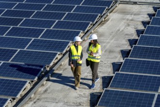 Two women engineers wearing hard hats and high visibility vests walking and discussing work on a