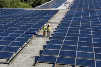 Engineers in hard hats and vests performing an inspection of a rooftop solar power plant, ensuring