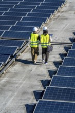 Two renewable energy engineers, wearing hard hats and reflective vests, walking along a rooftop