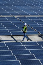 Engineer wearing safety helmet and vest, holding digital tablet and talking on phone while walking