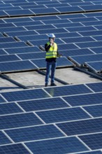 Engineer in hard hat and safety vest on commercial rooftop amid solar panels, using mobile phone