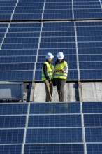 Female engineers wearing hard hats and high visibility vests discussing data on a digital tablet