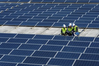 Team of diverse engineers wearing white hard hats and high visibility vests inspecting an array of