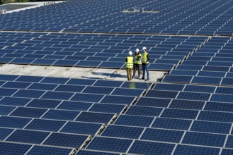 Engineers wearing safety vests and hard hats are standing on a large rooftop solar farm, reviewing