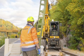 Construction worker with helmet looking at excavator working on rails, autumn environment, signal
