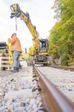 Excavator working on track, construction worker checking equipment, focus on rails, autumn