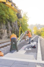 Workers install object on railroad tracks, surrounded by autumn trees, signal building on the