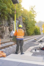 Workers wearing protective clothing on railroad tracks surrounded by autumn trees, signal building