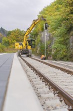 Yellow excavator on railroad tracks, surrounded by autumn trees, signal building on the Hermann