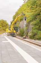 Yellow construction machine works on railroad tracks in a wooded area, Signalbau an der Hermann
