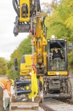 Close-up of an excavator with a worker, autumnal environment on railway tracks, signal construction