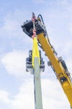A yellow crane lifts a metal structure, blue sky in the background, signalling at the Hermann