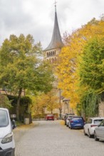 Church tower towers over an autumnal paved road with cars, Sindelfingen, Böblingen district,