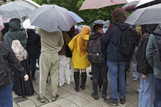 Young spectators with umbrellas in back view, woman with bright yellow rain jacket in between,