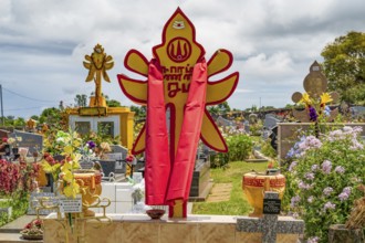 A bright red and yellow Hindu tombstone with religious symbols and a draped cloth stands as a sign