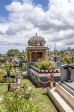A colorful, richly decorated Hindu shrine with a small temple roof in the cemetery stands between
