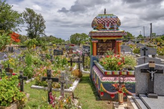 A colorful, richly decorated Hindu shrine with a small temple roof in the cemetery stands between
