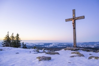 Christian cross on the peak of Mount Lusen with the view over the hills of the bavarian forest at