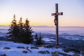 Christian cross on the peak of Mount Lusen with the view over the hills of the bavarian forest at