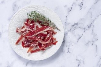 Ham of duck breast, dried duck fillet, with a sprig of thyme, white plate, on a marble table