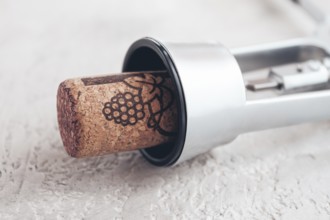 A shiny silver corkscrew rests on a light textured surface, with a wine cork partially inserted,