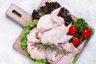 Raw quail meat, three quail carcasses, on a wooden chopping board, garnished with lettuce and herbs