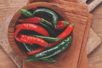 Vibrant red and green chili peppers rest in a wooden bowl, placed on a textured brown cloth atop a
