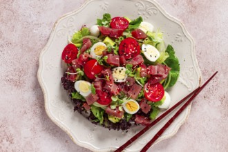 Salad with fresh tuna, cherry tomatoes and quail eggs and avacado, served with chopsticks