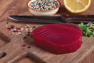 Fresh tuna steak, on a wooden cutting board, with lemon and sesame seeds, on a wooden table