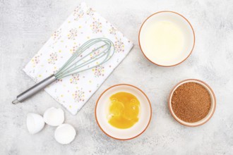 On the dessert preparation table, there are bowls with egg white, and yolk, cane sugar, and a whisk