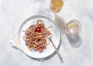 A plate with spaghetti topped with tomato sauce and cherry tomatoes sits on a light table. A glass