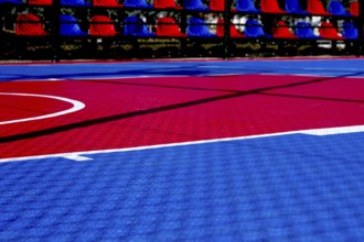 The basketball court features a striking red and blue design illuminated by bright sunlight. The