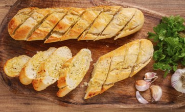Garlic bread, baguette with garlic butter and herbs, on a wooden board, with herbs and garlic