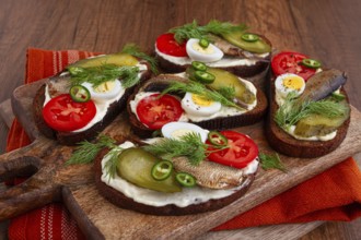 Sandwiches on rye bread with sprats, quail eggs, fresh tomatoes and pickled cucumber, on a wooden