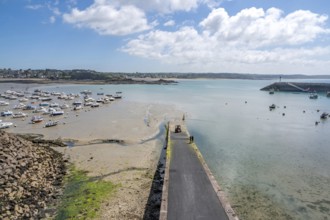 A long, dark pier juts out into the shallow harbor area, where numerous sailing and fishing boats