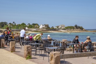 Numerous guests sit at small tables on the sunny terrace of the Grand Hotel Du Port Blanc on the