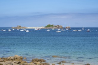 In the turquoise-blue waters of the English Channel, motor boats and sailboats anchor off small,