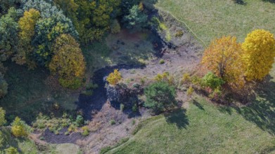 A picturesque view of a hilly landscape in autumn, with colorful deciduous trees, a small clearing