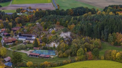 A picturesque village is surrounded by colorful trees in autumn. A castle ruin is nearby, while the