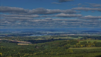 The picture shows a picturesque landscape with green forests, rolling hills and a river in the