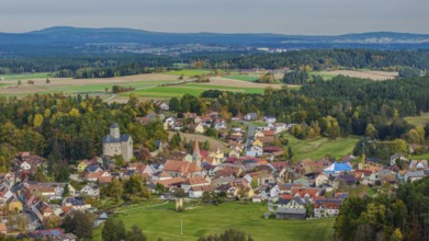 A gentle hilly landscape surrounds a small village with colorful houses and an old castle. The