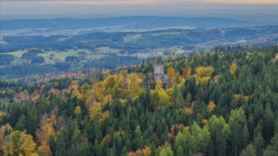 The ruins of Weissenstein Castle rise above a colorful forest whose leaves glow in autumn. The