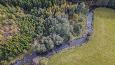 The river snakes through the countryside, surrounded by green trees and golden yellow leaves. The