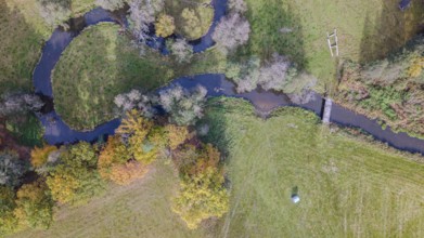 The scene shows a quiet river flowing through a picturesque meadow. Autumn colors of the trees and