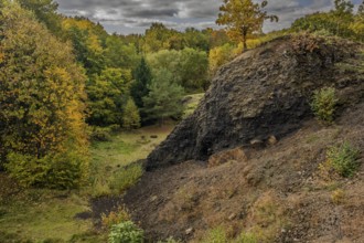 The scene shows an extinct volcano in autumn. Colourful trees surround a dark slope, while the sky