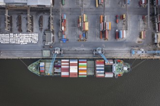 Aerial view of a cargo ship docked at a port with colorful containers and industrial surroundings.