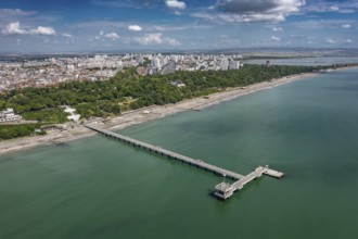 Aerial view of a long pier extending into the sea with cityscape in the background. Aerial view to